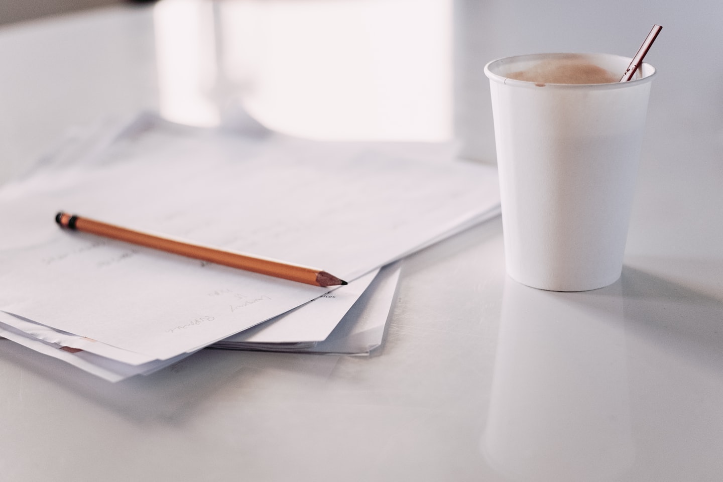 A pencil sits on a stack of papers next to a coffee cup.