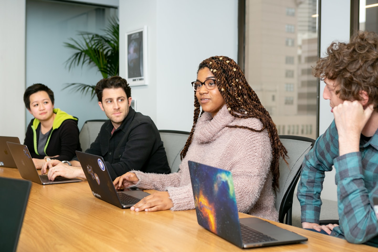 Diverse professionals collaborating around a wooden conference table with laptops.