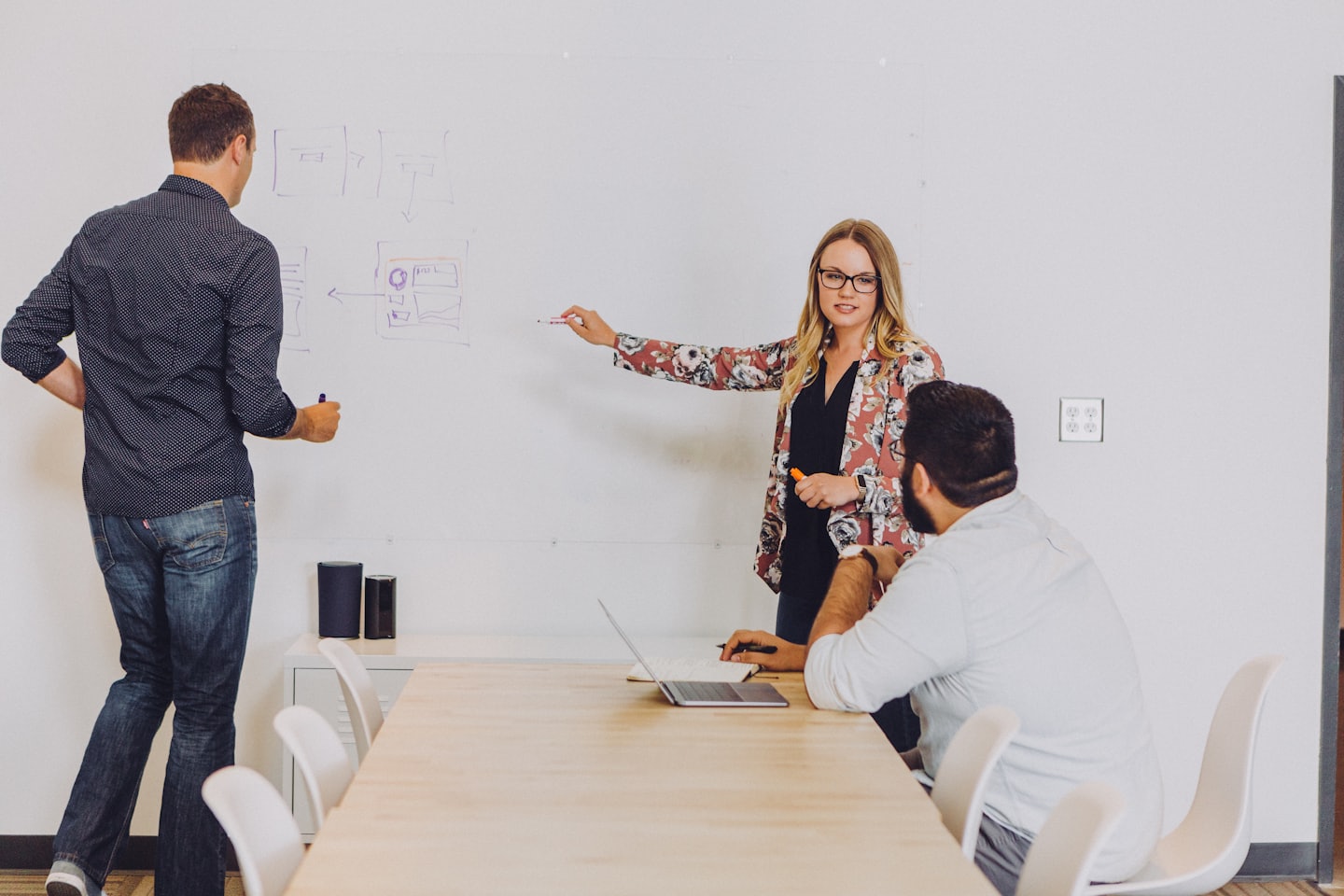 Professionals collaborating around a conference table discussing whiteboard diagrams.