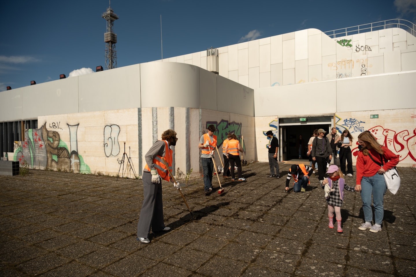 Volunteers in safety vests sweep debris outside a graffiti-covered building.