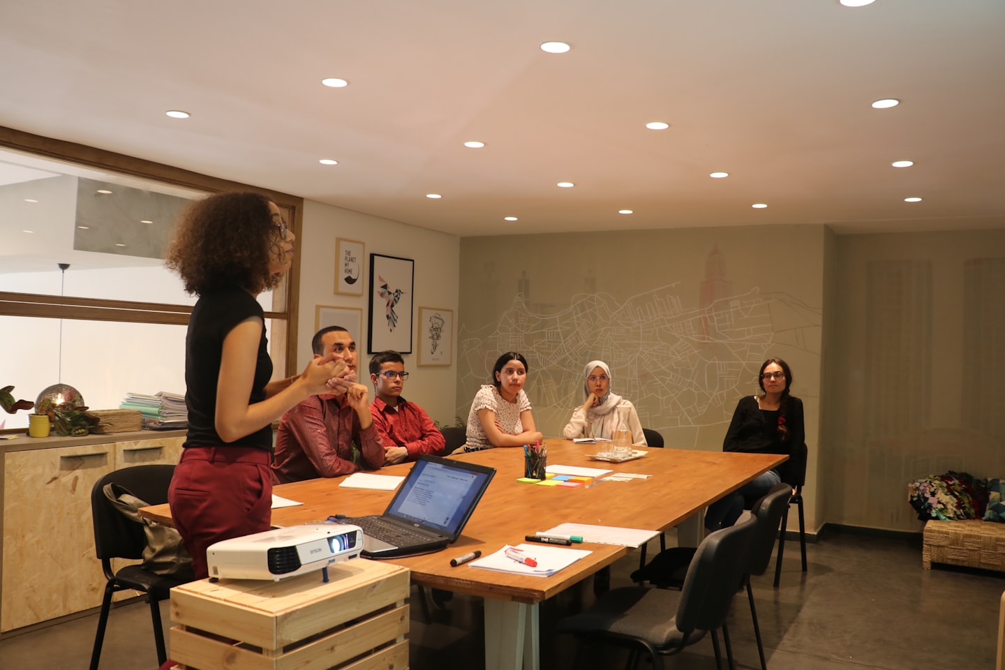 Woman leads a meeting around a large wooden table.