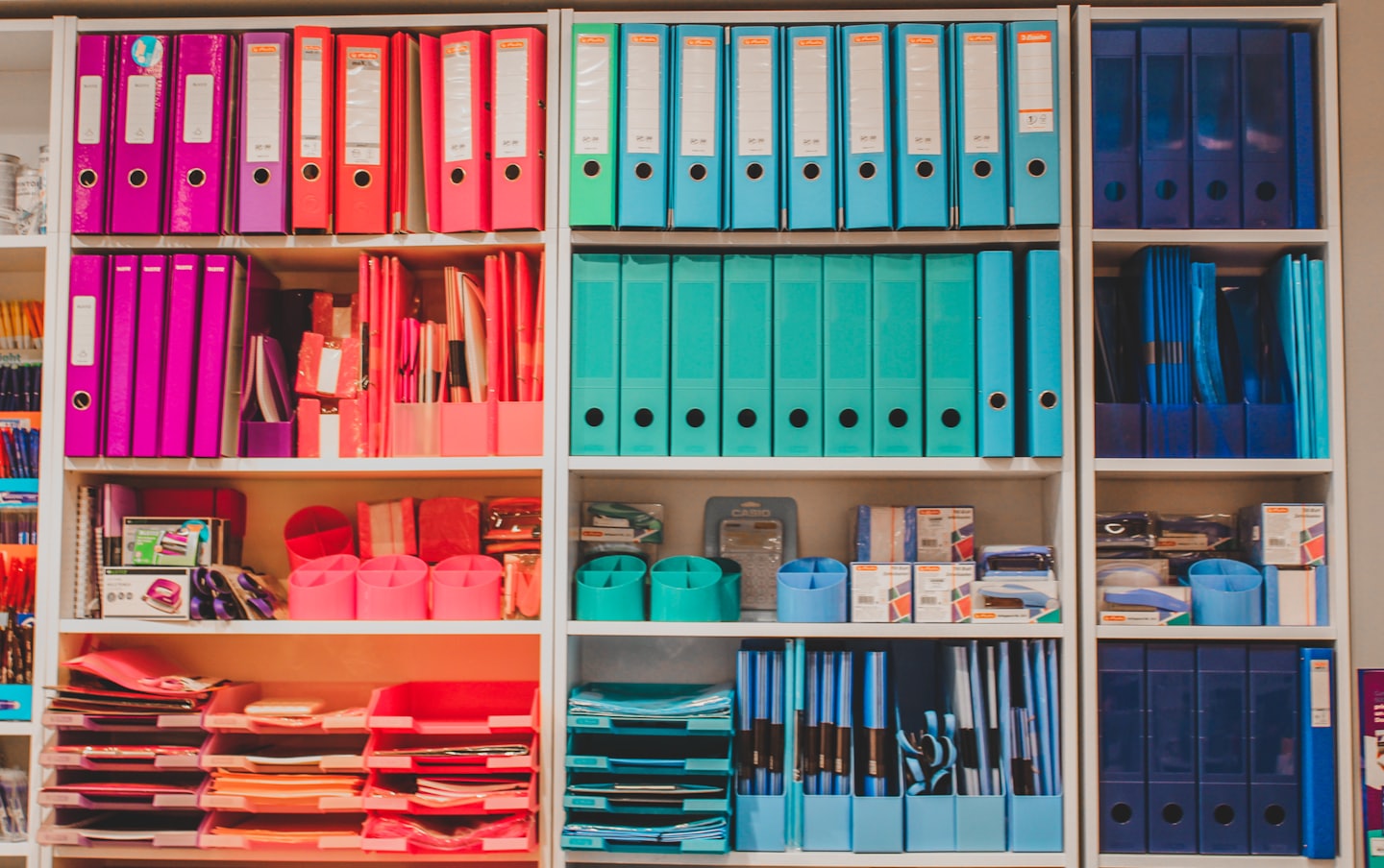 Organized shelving unit filled with rows of colorful office supplies.