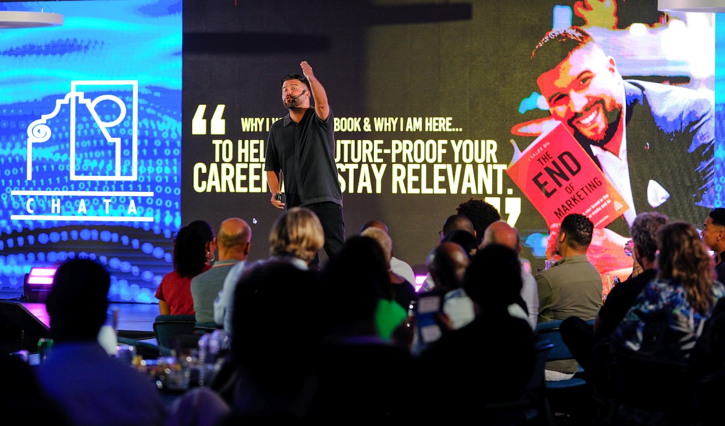 Speaker presents to an audience on a stage with large screens.