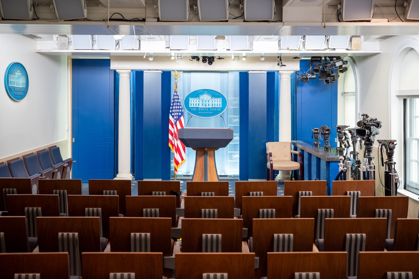 Empty press briefing room featuring a central podium and blue backdrop.
