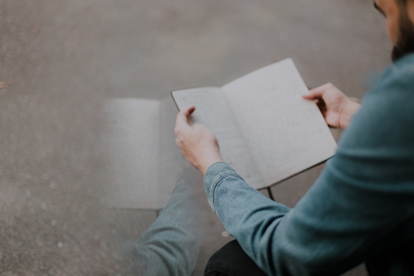 Hands hold an open notebook outdoors while writing notes.