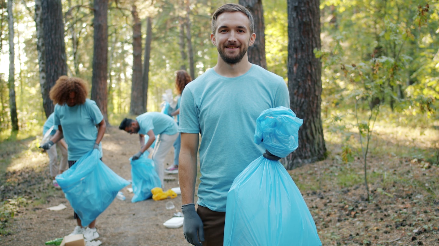 Diverse volunteers cleaning up a sunny forest trail together.